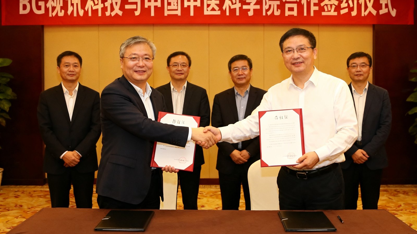 BG视讯科技与中国中医科学院合作签约仪式现场，双方代表握手并展示合作协议文本